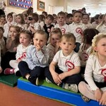 Dzieci siedzą ubrane w stroje galowe, z przypiętymi kotylionami.